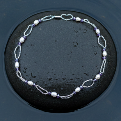 Zoetwater parelketting met witte parels, paarse glaskristallen en magneetslotje liggend op steen in water | Pacio