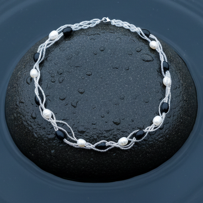 Zoetwater parelketting met witte parels en zwarte glaskralen liggend op steen in water | Twine Pearl Black Glass