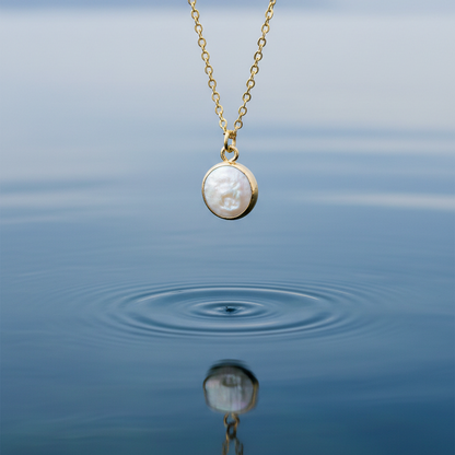 Detail van witte zoetwater parelketting met hanger hangend boven blauw water | White Coin Pearl Gold Small