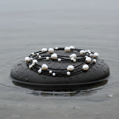 Lange zoetwater parelketting met witte parels en zwarte glaskraaltjes ligt opgerold op natte steen | White Pearl Black Sweater
