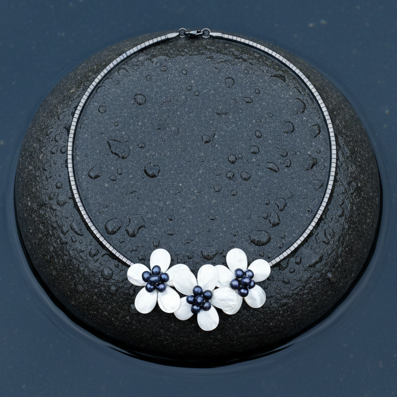 Detail van zoetwater parelketting met blauw zwarte parels en wit parelmoer in de vorm van een bloem met zilver edelstaal liggend op steen in water | Florien B