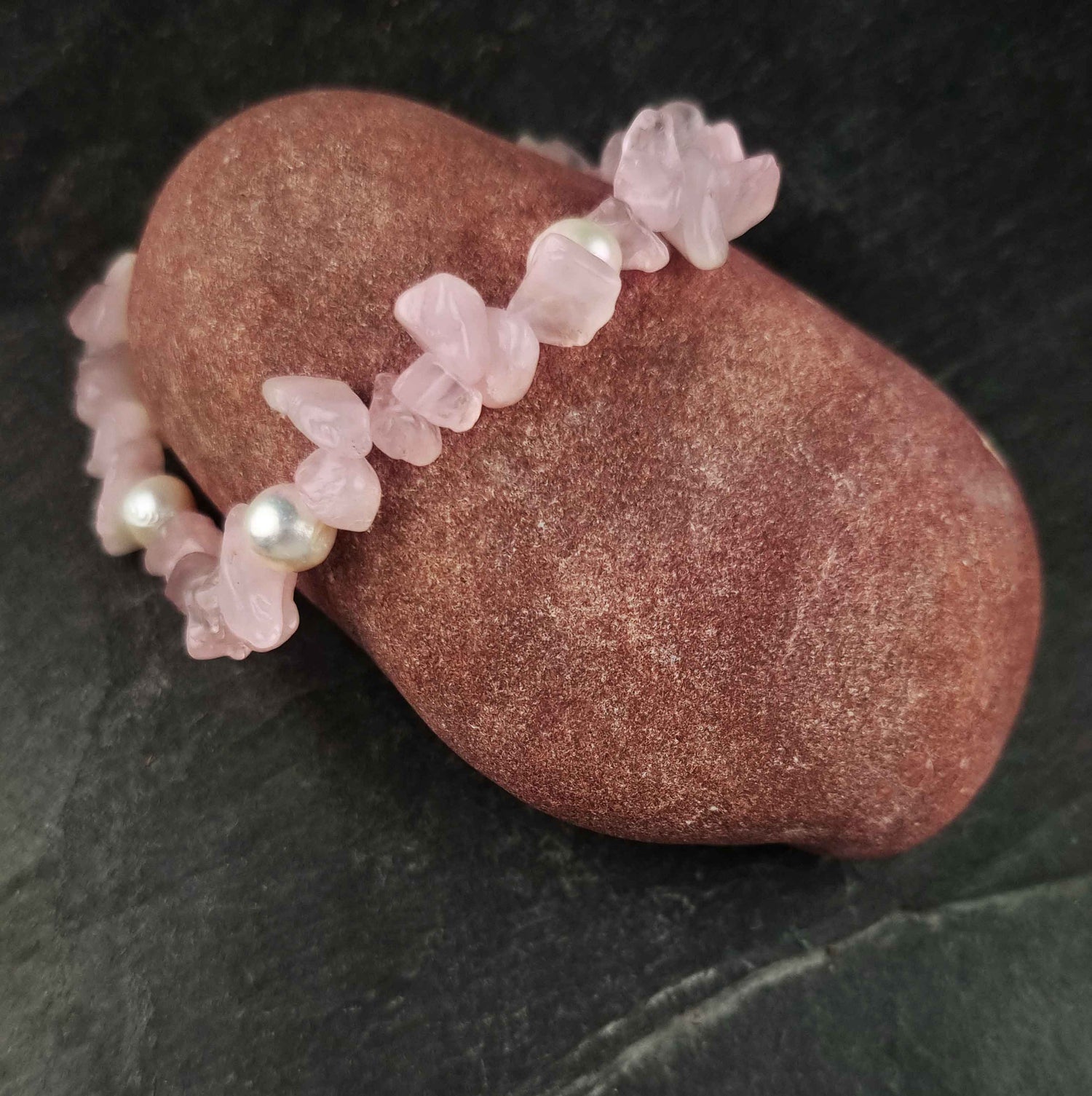 Wit zoetwater parel armband met roze edelstenen rozenkwart liggend op rode steen, elastisch | Pearl Rose Quartz Chip