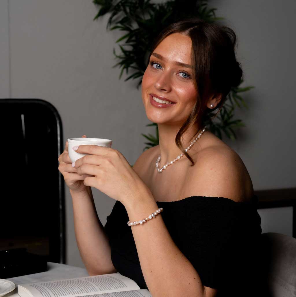 Handgeknoopte zoetwater parel set bestaande uit parelketting en parel armband met witte, zalm en roze parels en sterling zilver (925) op model met boek en koffie | set Pearl Colors Small