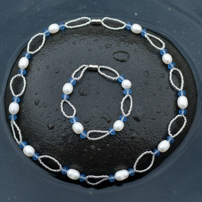 Zoetwater parel set bestande uit een parelketting en parel armband met witte parels, blauwe glaskristallen en magneetslotje liggend op steen in water | set Blacio