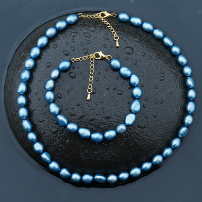 Blauw zoetwaterparel ketting en armband met goud edelstalen slotje is volledig handgeknoopt met barok parels  en ligt op een steen in water | Blair