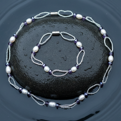 Zoetwater parel set bestaande uit een parelketting en parel armband met witte parels, paars glaskristallen en magneetslot liggend op steen in water | set Pacio