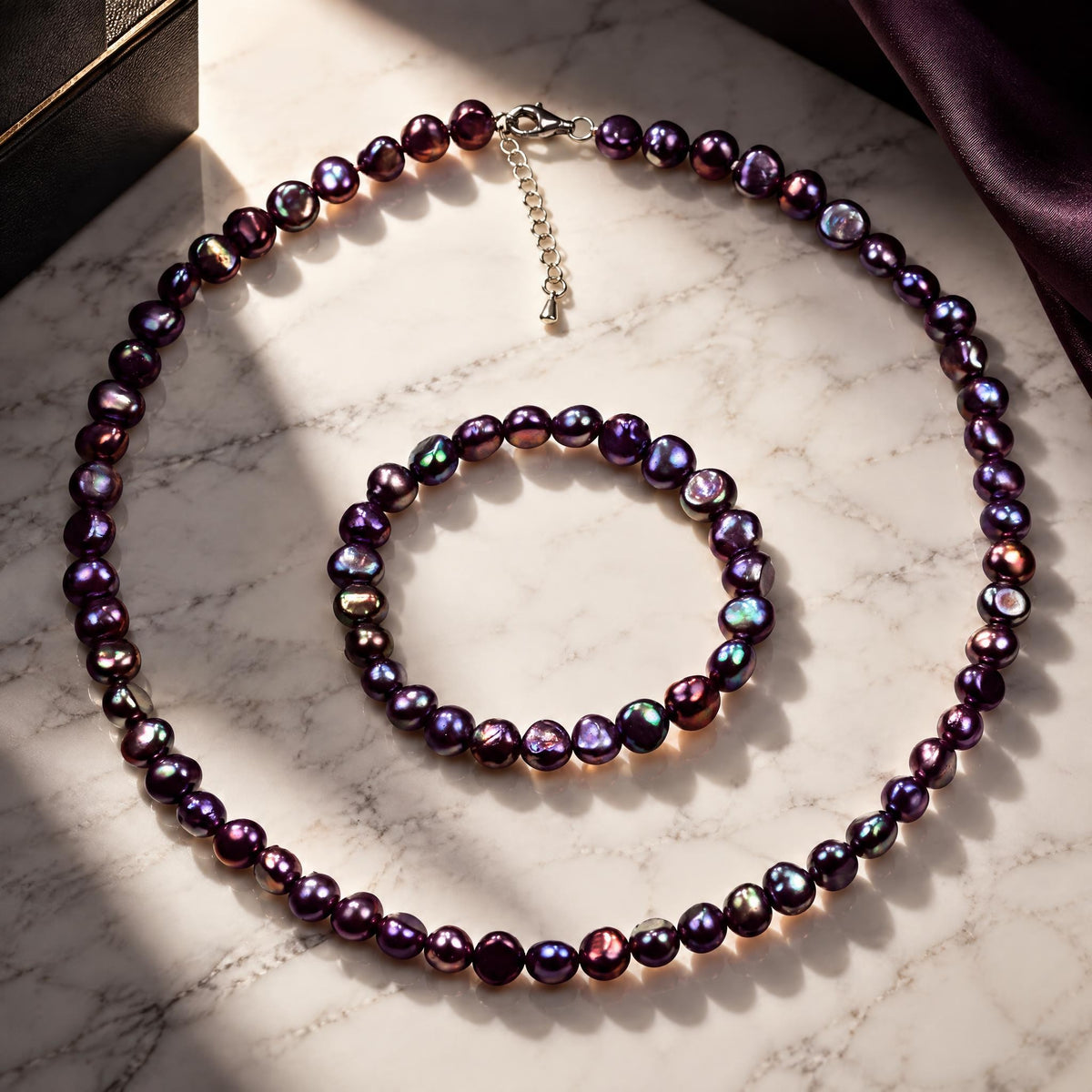 Zoetwater parel set bestaande uit een parelketting en parel armband met paars blauwe parels en gerhodineerd zilver liggend op marmer | set Peaca