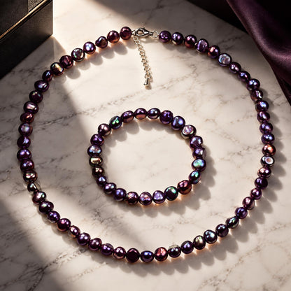 Zoetwater parel set bestaande uit een parelketting en parel armband met paars blauwe parels en gerhodineerd zilver liggend op marmer | set Peaca