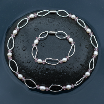 Zoetwater parel set bestaande uit een parelketting en parel armband met witte parels, roze glaskristallen en magneetslot liggend op steen in water | set Rocio
