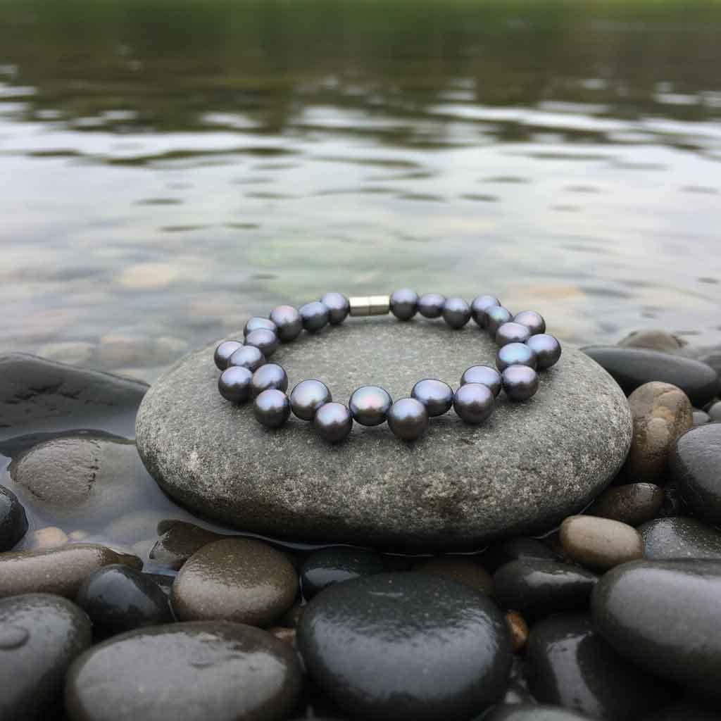 Zoetwater parel armband met blauw-paarse parels en magneetslot liggend op steen bij water | Gent