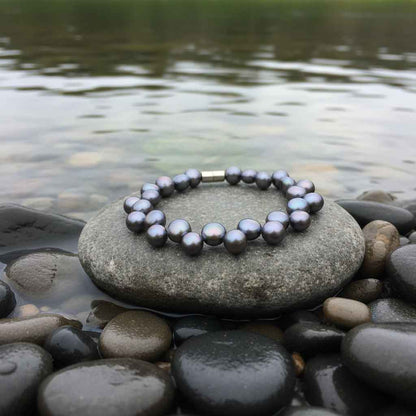 Zoetwater parel armband met blauw-paarse parels en magneetslot liggend op steen bij water | Gent