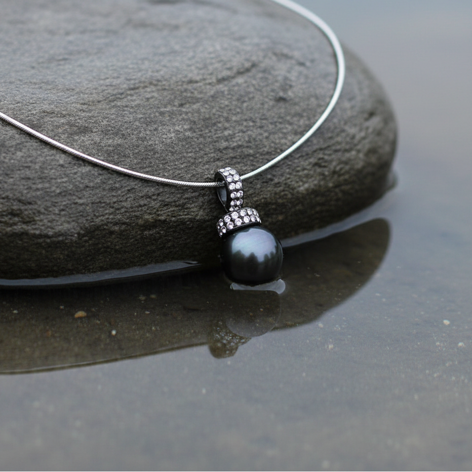 Mother of pearl parelketting met zwart groene parel en stras steentjes liggend op steen in water close up | Balanie