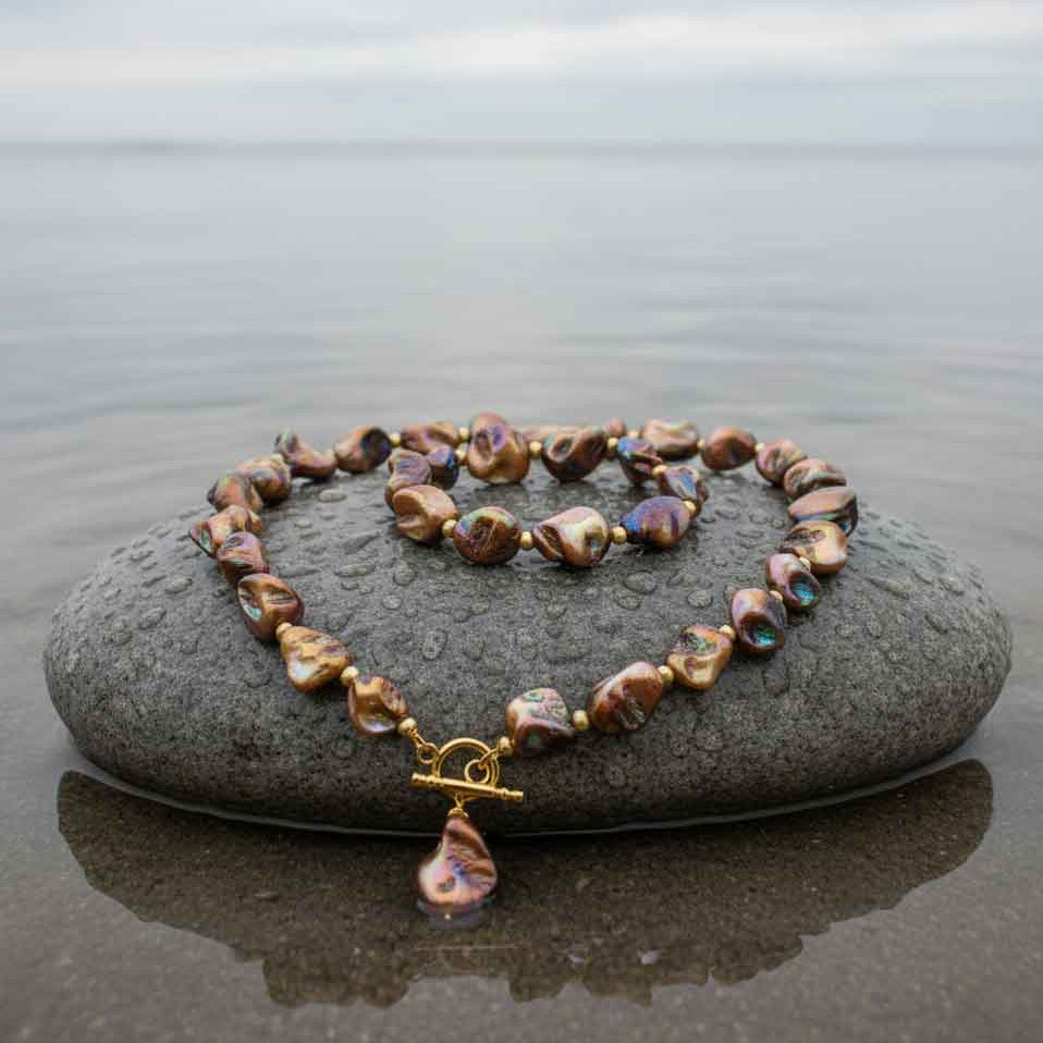 Bruin parelmoeren schelpen set met ketting en armband en goud edelstaal liggend op een natte steen | set Shell AB Brown Gold