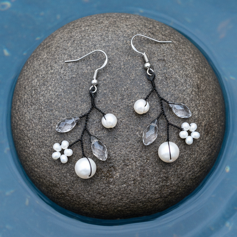 Zilveren fish hook oorbellen met witte parels en heldere kristallen op steen met helder blauw water