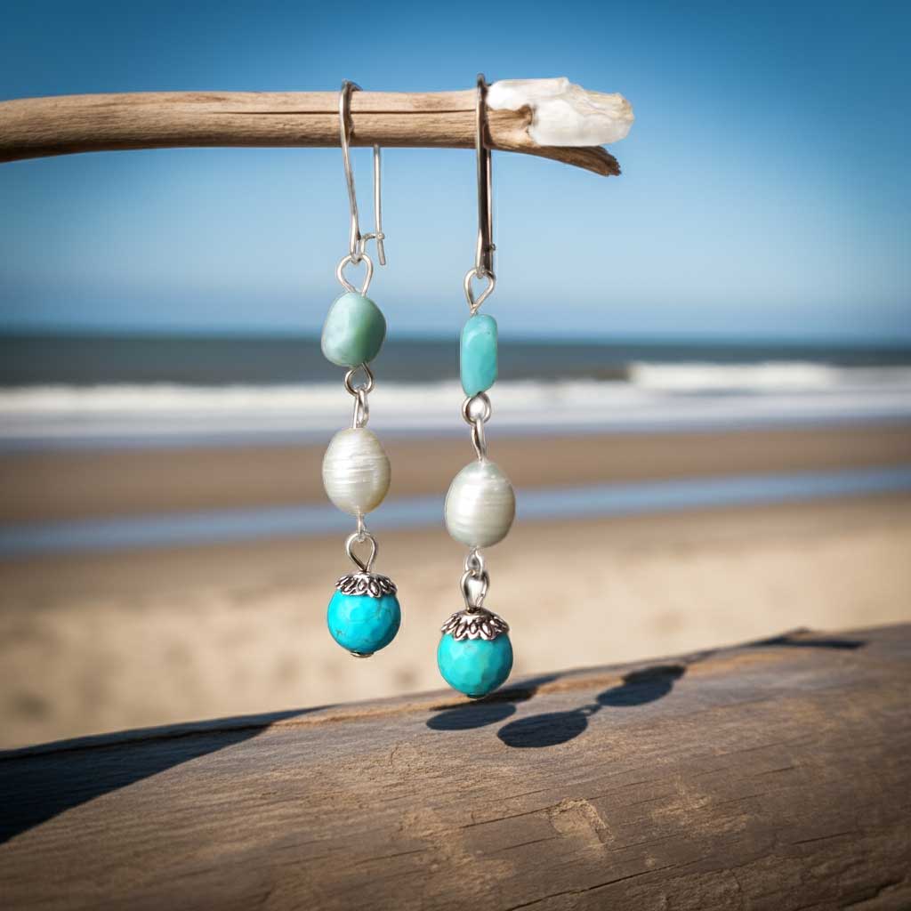 Zoetwater parel oorbellen met witte parels, blauwe edelsteen larimar en zilver edelstaal hangend aan takje met achtergrond strand | Oorbellen Lalita Larimar