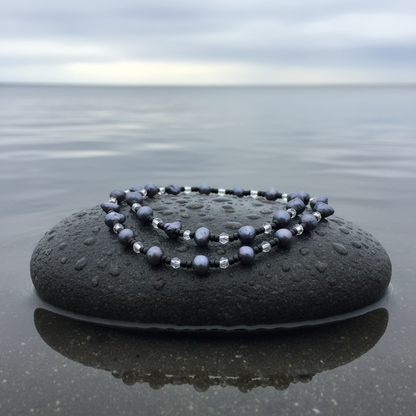 Lange zoetwater parelketting met zwart blauwe parels liggend op natte steen | Izora