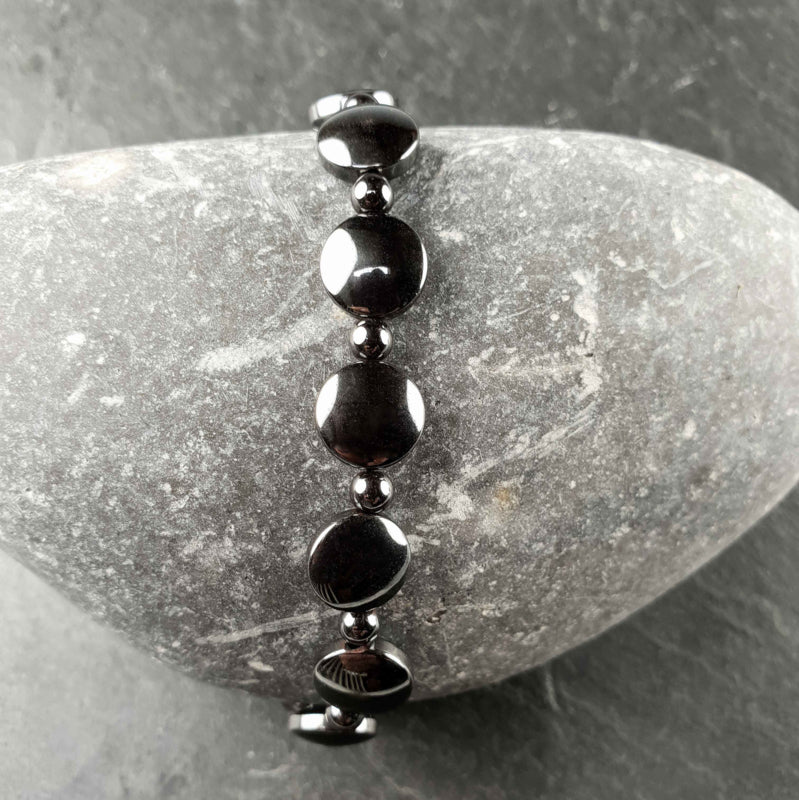 Zwart edelstenen armband met hematiet liggend op kei | Elastisch | Hematite Coin