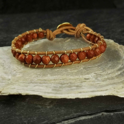 Bruin edelstenen armband met goudvuur / goudsteen en leer liggend op witte schelp | Wrap Gold Sand