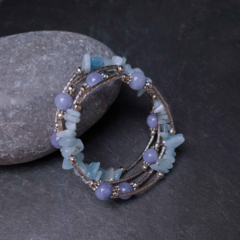 Blauw edelstenen wikkelarmband met aquamarijn en aventurien liggend tegen steen, vooraanzicht