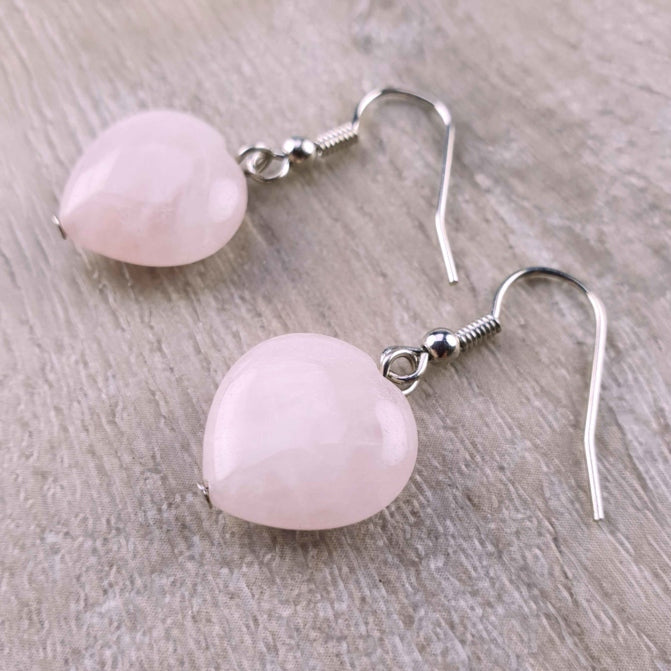 Roze edelstenen oorbellen met rozenkwarts in hartjes vorm en sterling zilver (925) liggend op hout | Rosé Love