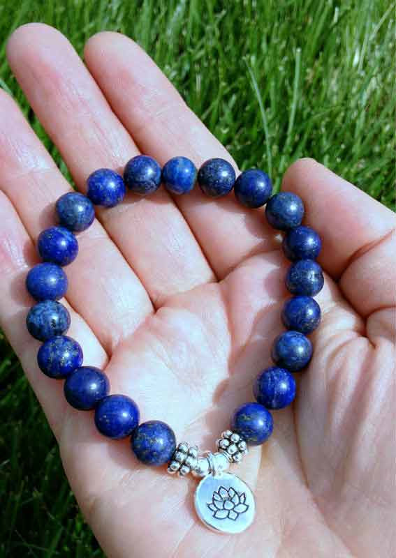 Blauw edelstenen armband met zilver lotus bedeltje liggend in hand, elastisch edelstenen armband