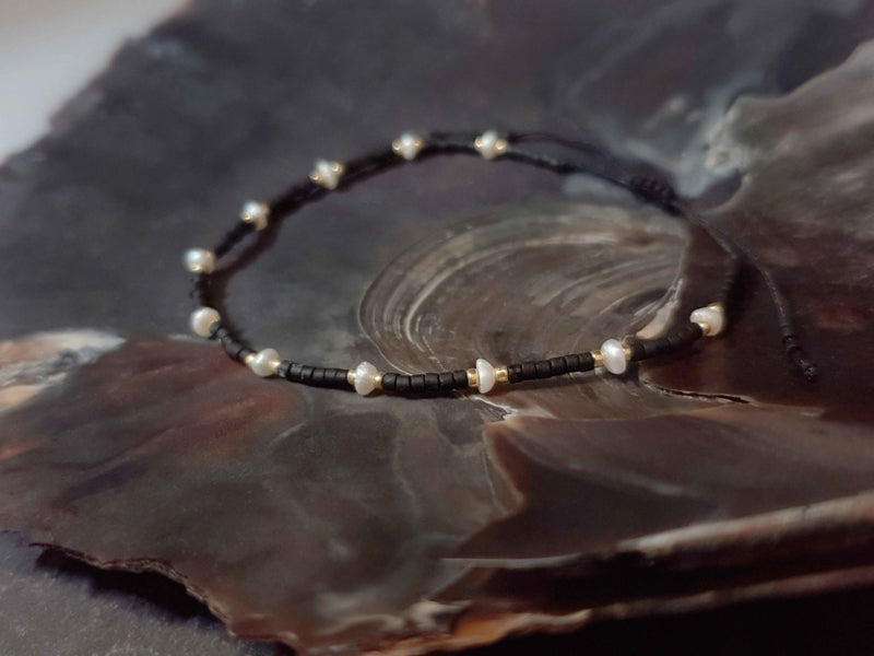 Wit zoetwater parel schuif armband met zwarte en gouden kraaltjes liggend in schelp | Mini Pearl Bead Black