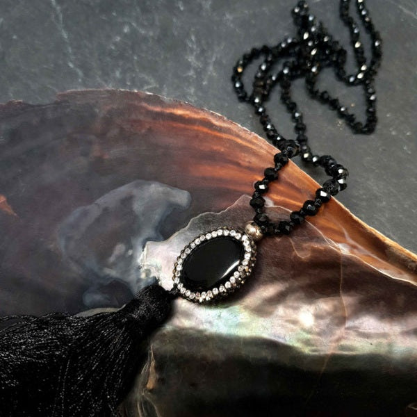 Lange zwarte handgeknoopte edelstenen ketting met agaat, stras steentjes en kwastje liggend in schelp | Long Bright Black Agate Tassel