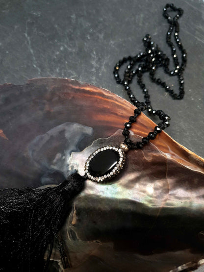 Lange zwarte handgeknoopte edelstenen ketting met agaat, stras steentjes en kwastje liggend in schelp | Long Bright Black Agate Tassel