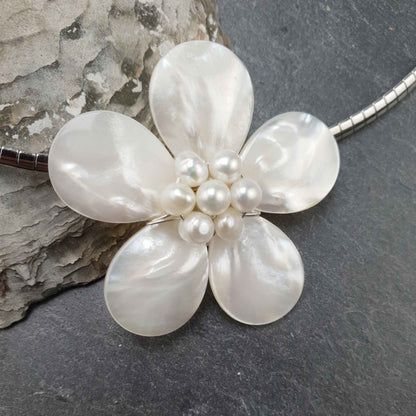 Detail van zoetwater parelketting met witte parels, wit parelmoer in de vorm van een bloem en zilver edelstaal liggend tegen schelp | Fleury W