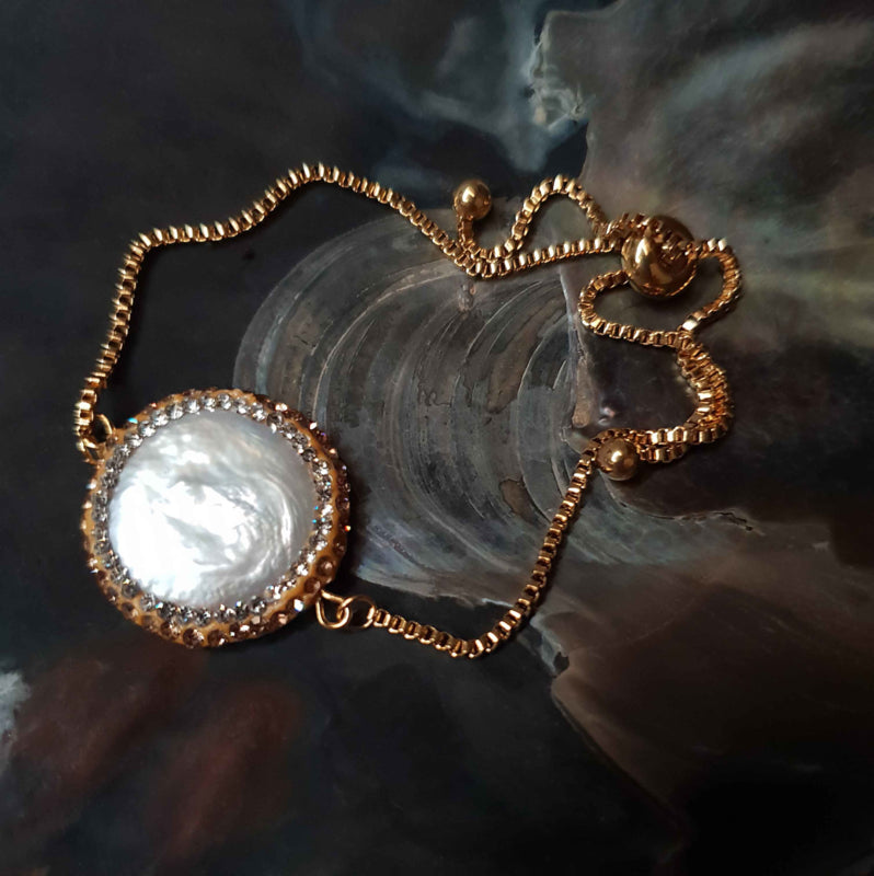Wit zoetwater parel armband met goud edelstaal, stras steentjes en een schuifslotje liggend in schelp | Bright Golden Pearl