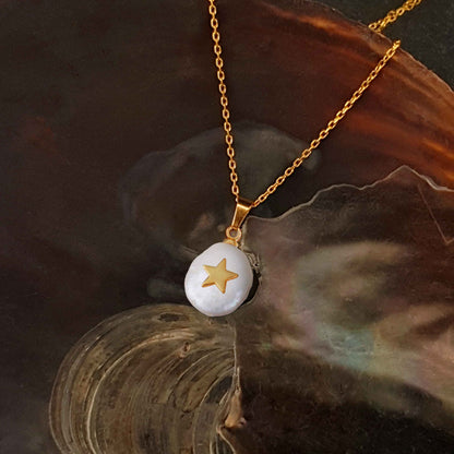 Detail van zoetwater parelketting met witte parel hanger met gouden ster en goud edelstaal liggend in schelp | Coin Pearl Golden Star