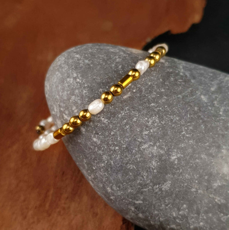 Wit zoetwater parel wikkelarmband met edelsteen goud hematiet liggend tegen kei | Cadeau set zoetwater parel armband Morse Code BFF Pearl Gold