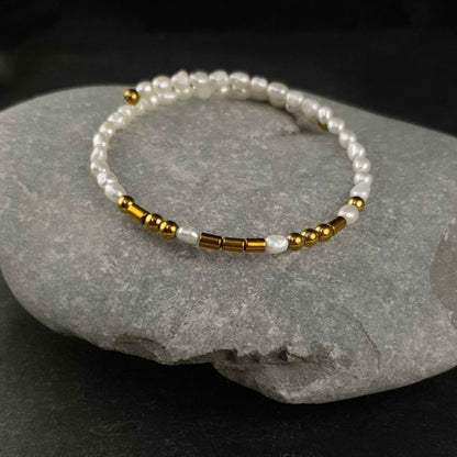 Wit zoetwater parel wikkelarmband met verborgen boodschap LOVE in Morse code met edelsteen goud hematiet liggend op kei  | Cadeau set zoetwater parel armband Morse Code LOVE Pearl Gold
