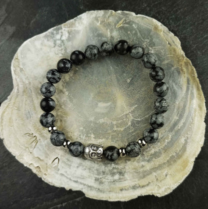 Edelstenen armband met zwart grijze edelsteen en zilver kleurige Boeddha | Elastisch liggend op witte schelp | Buddha Snowflake Obsidian