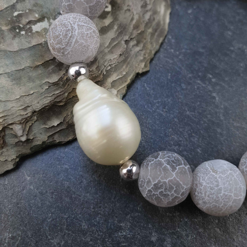 Detail van zoetwater parel armband met witte parel en grijze edelsteen agaat, elastisch liggend op leisteen| Frozen Grey Agate White Pearl