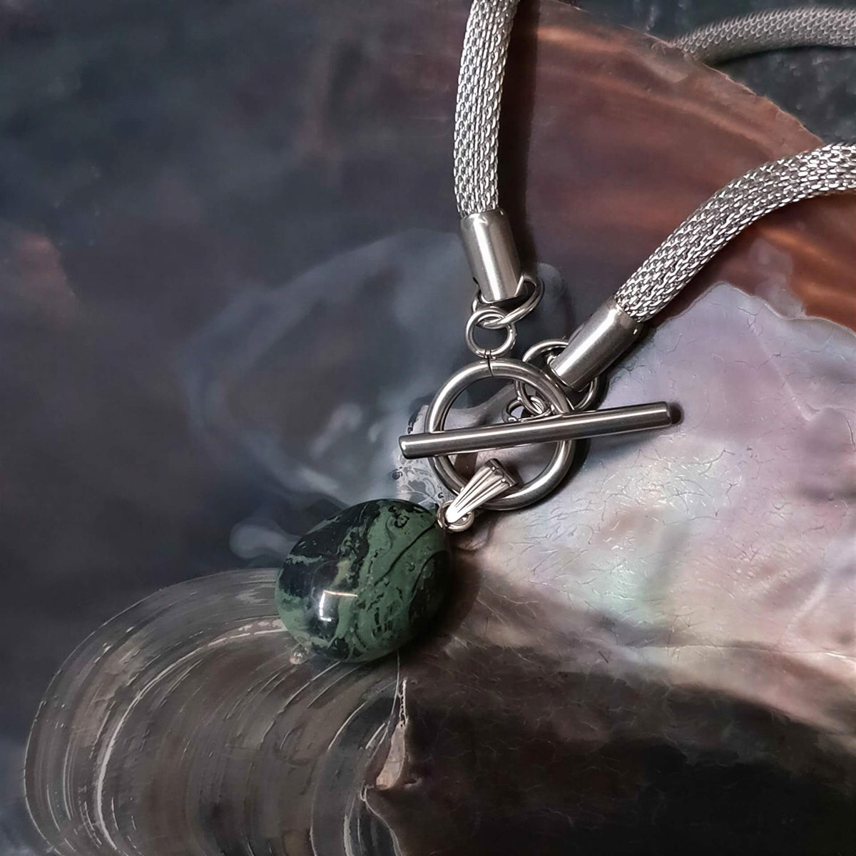 Detail van groen zwarte edelstenen ketting met nebula steen aan hanger en zilver edelstaal  liggend in schelp | Toggle Chain Nebula