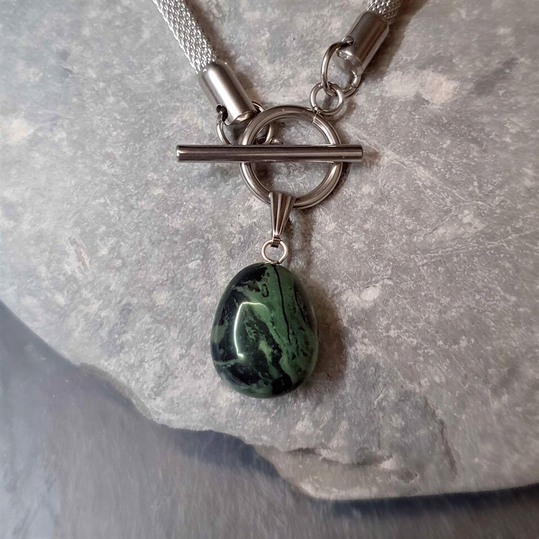 Detail van groen zwarte edelstenen ketting met nebula steen aan hanger en zilver edelstaal liggend op kei | Toggle Chain Nebula