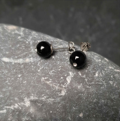 Zwarte edelstenen oorbellen met agaat en stras steentje , zwarte oorknopjes liggend op kei, zijaanzicht | Bling Black Agate