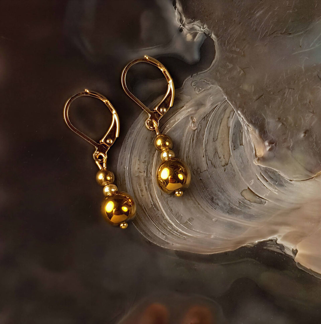 Edelstenen oorbellen met goud hematiet en goud edelstaal liggend in schelp | Bold Gold Hematite