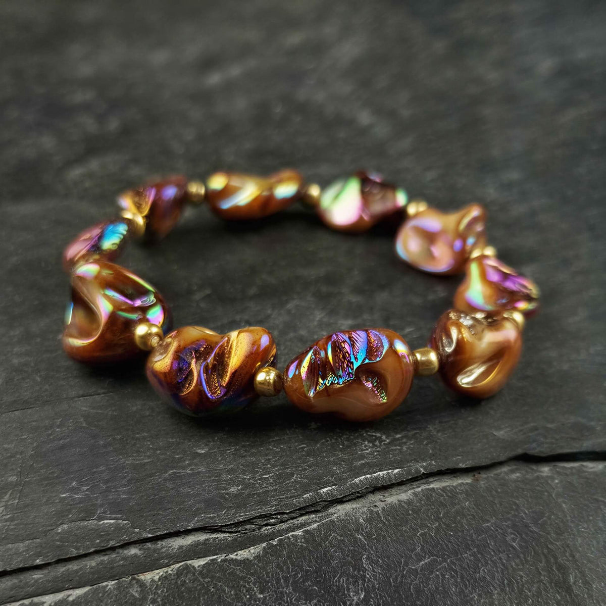 bruin elastisch parelmoeren armband met goud liggend op leisteen