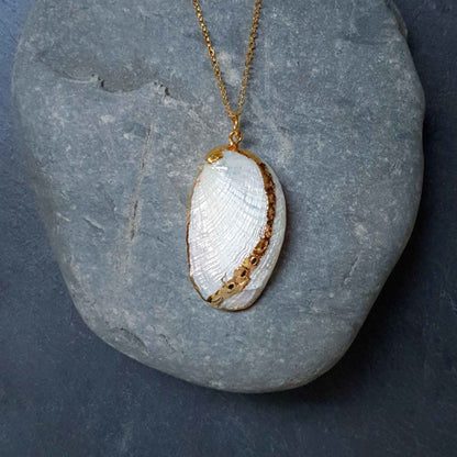 Detail van parelmoeren schelpen ketting met witte schelp en goud edelstaal liggend op kei | set White Shell Gold