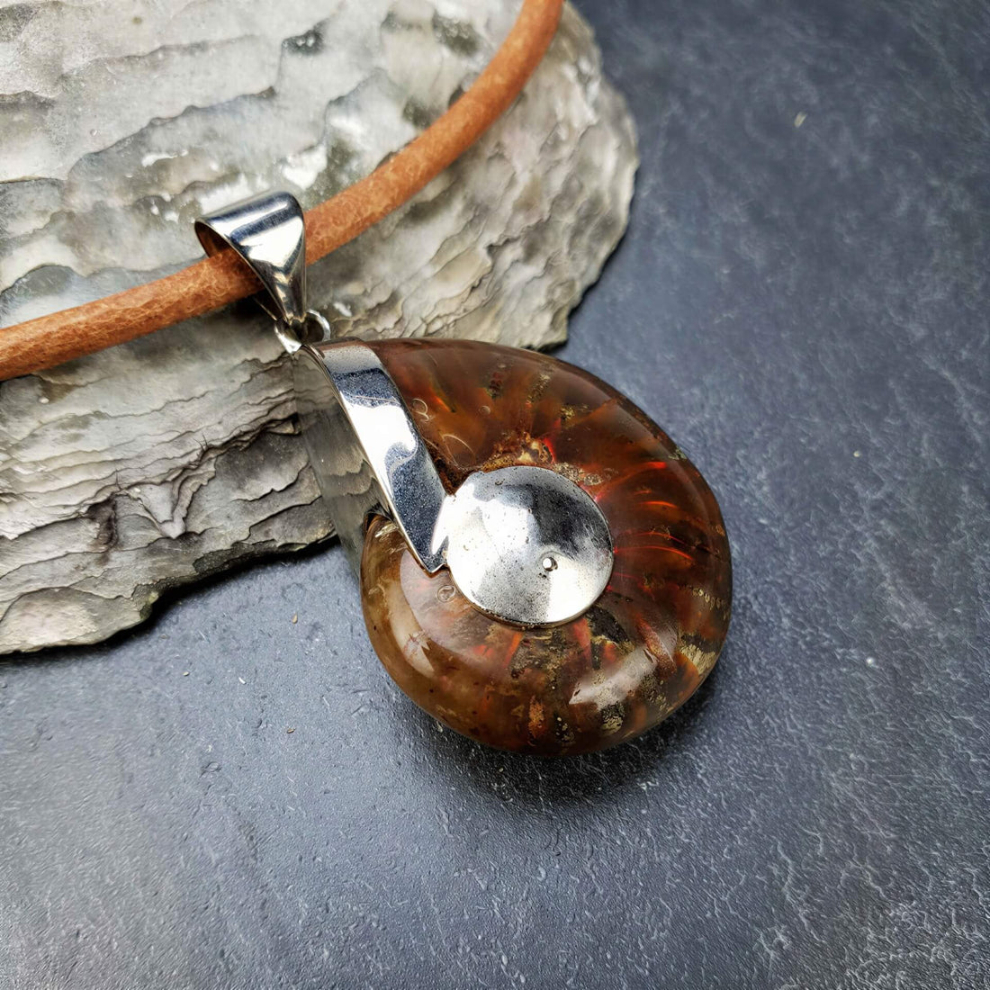Detail van schelpen ketting met een versteende nautulus schelp en leer liggend op leisteen | Fossiel