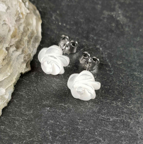 Witte parelmoeren oorknopjes in bloem vorm liggend op leisteen | White Shell Flower 8 mm
