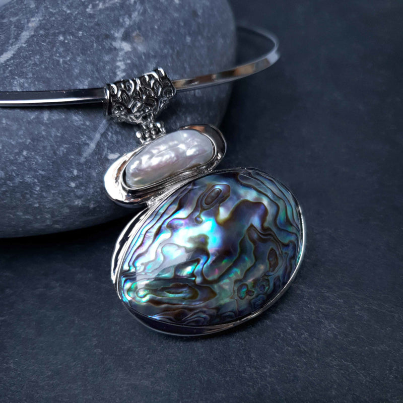 Detail van zoetwater parelketting met abaloon hanger liggend tegen kei | Biwa Abalone