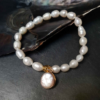 Wit zoetwater parel armband met rond bedeltje liggend tegen schelp | Golden Pearl Coin