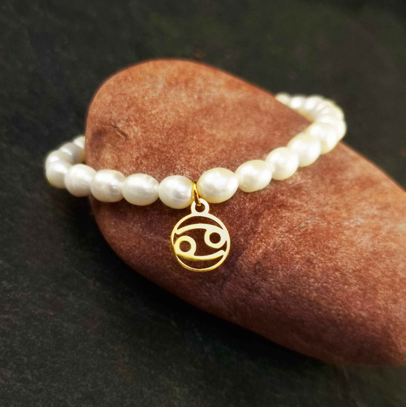 Wit zoetwater parel armband met goud edelstalen bedeltje van sterrenbeeld Kreeft liggend op rode steen | Gouden Sterrenbeeld Kreeft