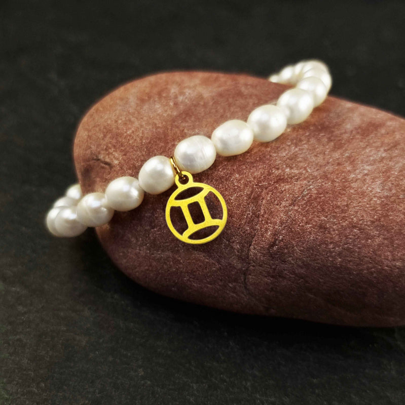 Wit zoetwater parel armband met goud edelstalen bedeltje van sterrenbeeld Tweeling liggend op rode steen| Gouden Sterrenbeeld Tweeling
