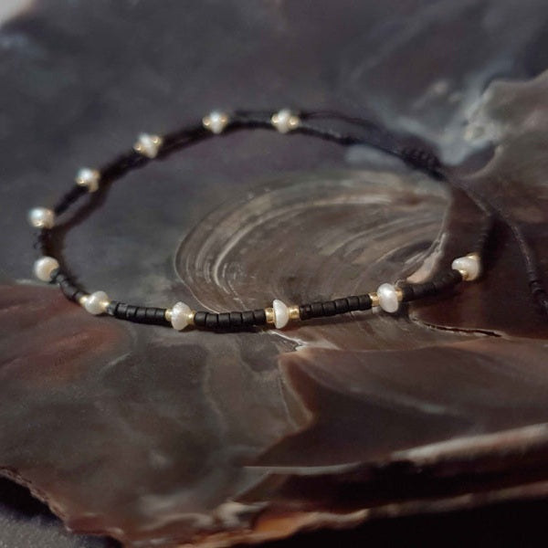 Wit zoetwater parel schuif armband met zwarte en gouden kraaltjes liggend in schelp | Mini Pearl Bead Black