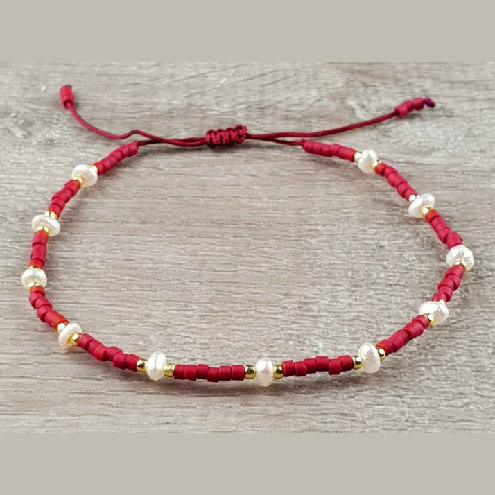 Wit zoetwater parel armband met rode en gouden kraaltjes en schuifsluiting liggend op hout | Mini Pearl Bead Red