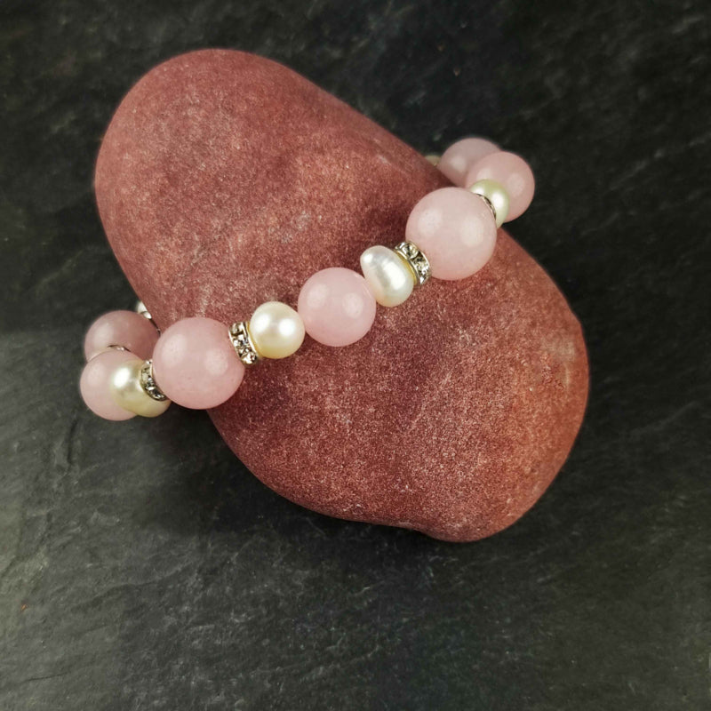 Wit zoetwater parel armband met roze edelstenen rozenkwart en stras steentjes , elastisch, liggend op rode steen | Bling Paerl W Rose Quartz
